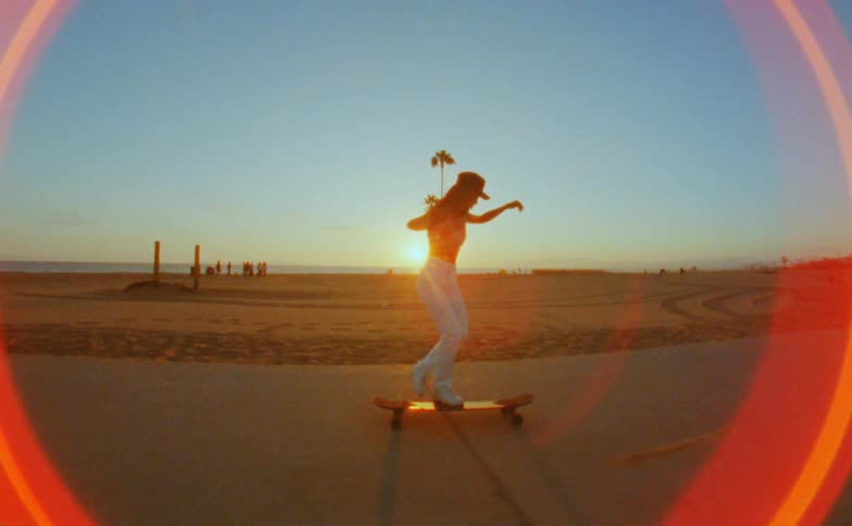 The sun is causing a bloom on the camera filming a woman on a skateboard