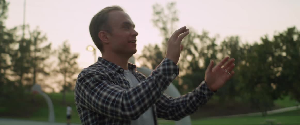 A man smiles and talks as he throws and catches a football at the park