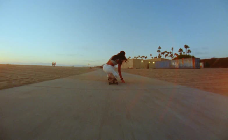 A teenage girl bends down and touches the road as she rides her skateboard