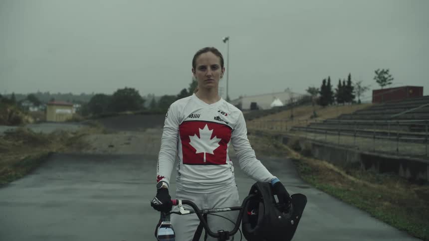 A woman holding a helmet is standing with her bike on a course