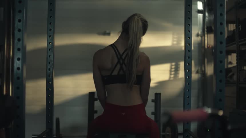 A woman is sitting on a bench in a gym doing stretches