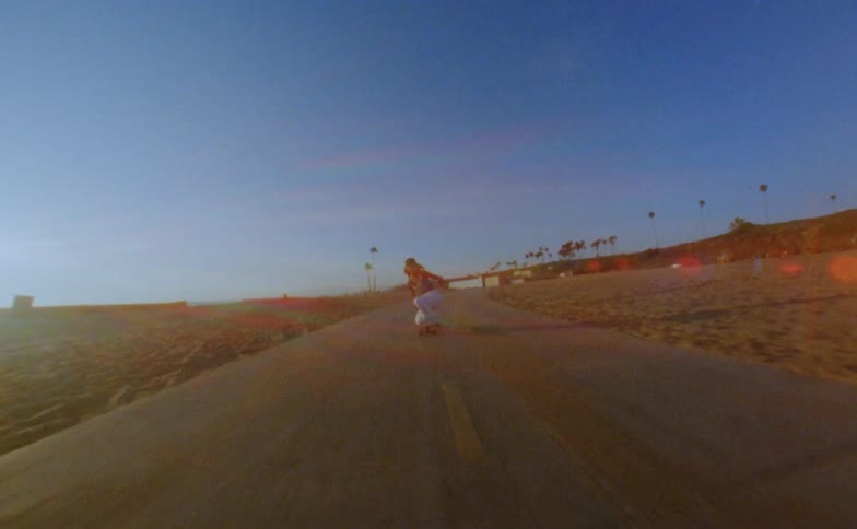 Young woman rides a skateboard on a road in the beach next to the ocean