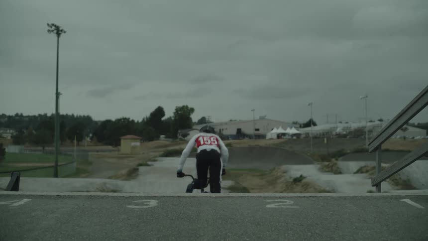 A person gets on a bike and starts on a course near some buildings