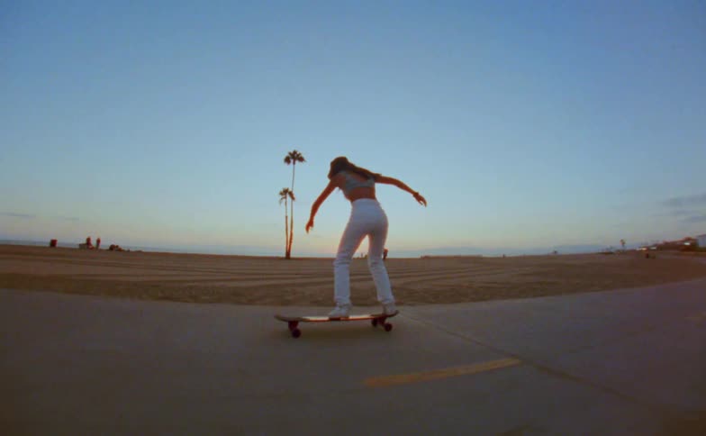 Young woman riding a skateboard on a road in the beach next to the ocean stumbles and falls