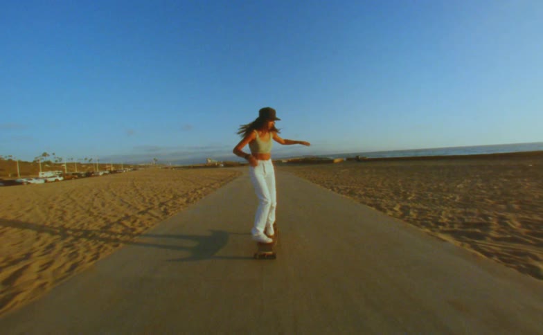 Teen girl skateboarding on asphalt in the middle of a beach while doing tricks on top of the skateboard