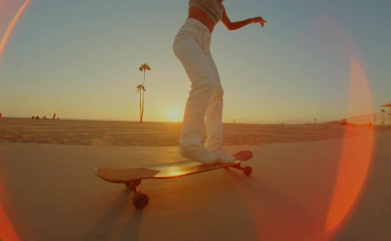 A woman moves her feet in dance like steps on a long board riding on a beach path