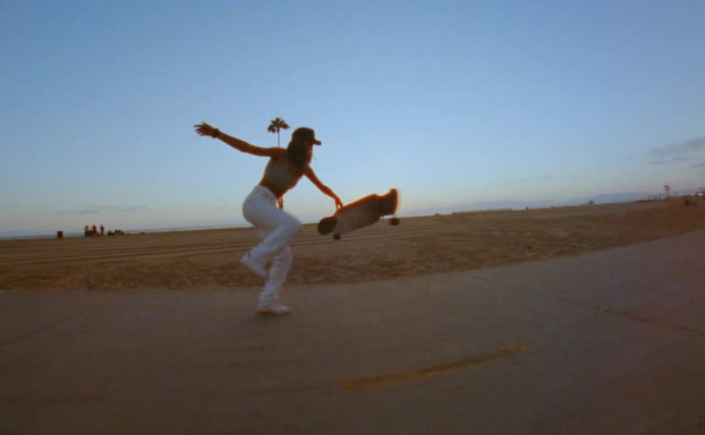 A young woman flips up a long board as she skateboards on a beach path