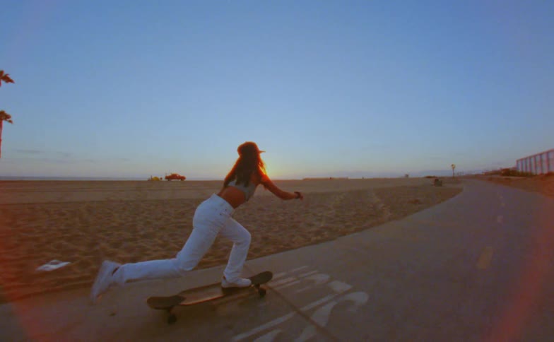 A young woman rides a skateboard on a path near the sand and beach