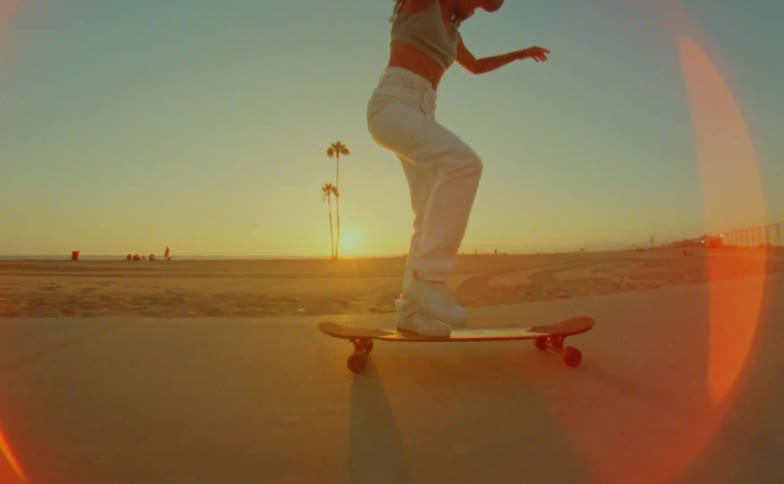 Young woman rides a skateboard on a road in the beach next to the ocean caught on vintage film
