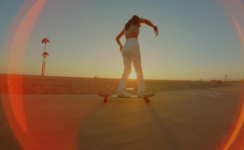 A woman spins and twirls while riding a long board skateboard on a beachside path