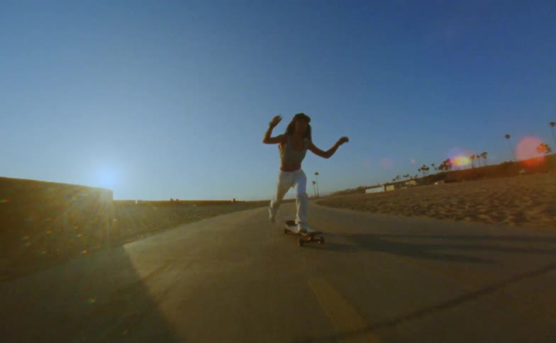Female skateboarder and person watching are both silhouetted by the sun