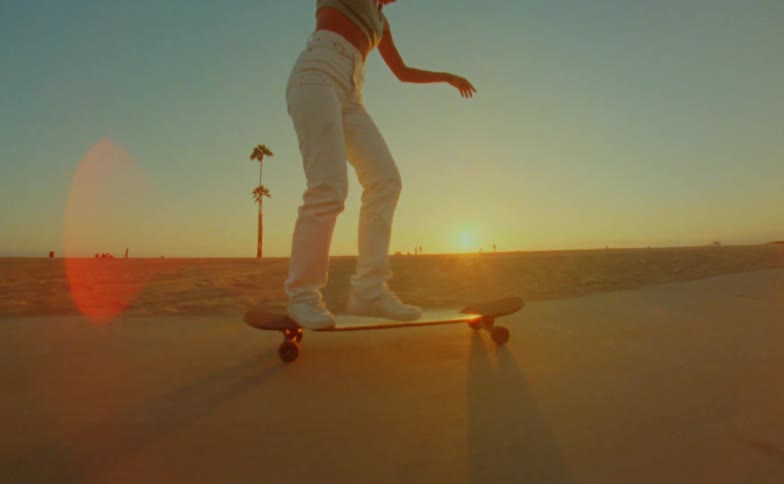 A woman is at the beach riding her skateboard as the sun sets