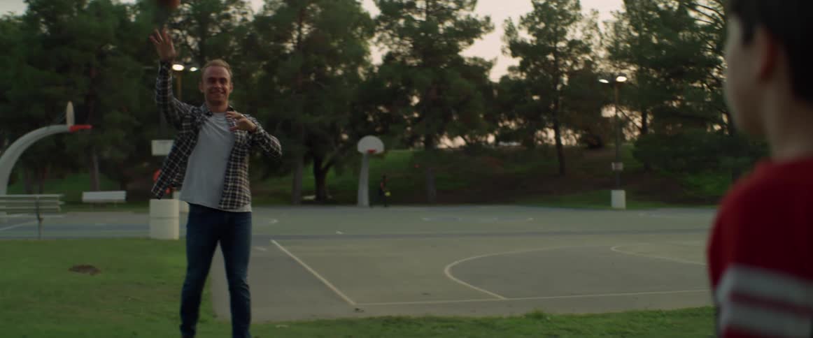 Father and son playing with a football in a public park near a basketball court