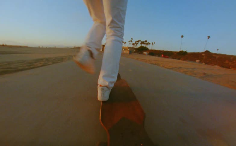 Young woman rides a skateboard on a road in the beach caught on vintage film
