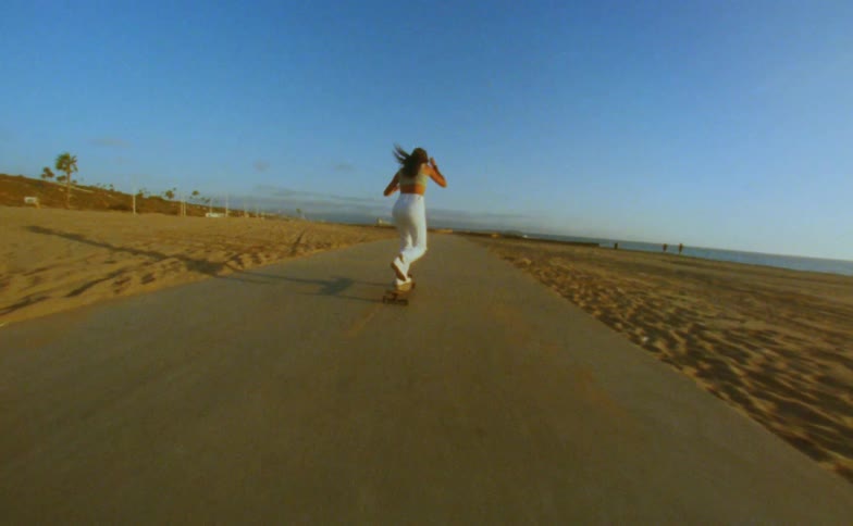 Woman runs forward and gets onto a skateboard on a road near a beach
