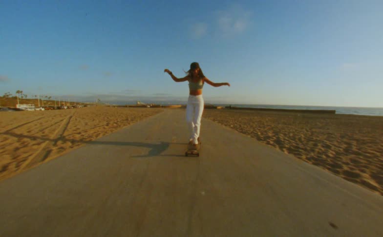 A woman is riding a skateboard along a path at the beach
