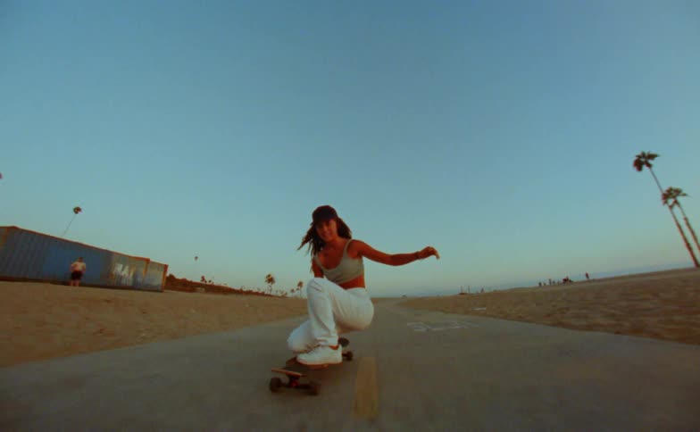 A woman is skateboarding down a sidewalk and does a trick at the end