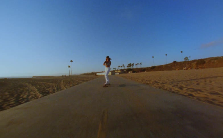 A teenage girl raises her arms in the air as she rides her skateboard on a road