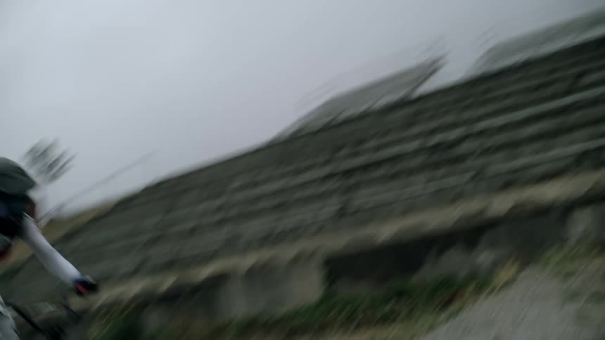 Person rides a bicycle at full speed on a gravel track on an overcast day next to a neighborhood