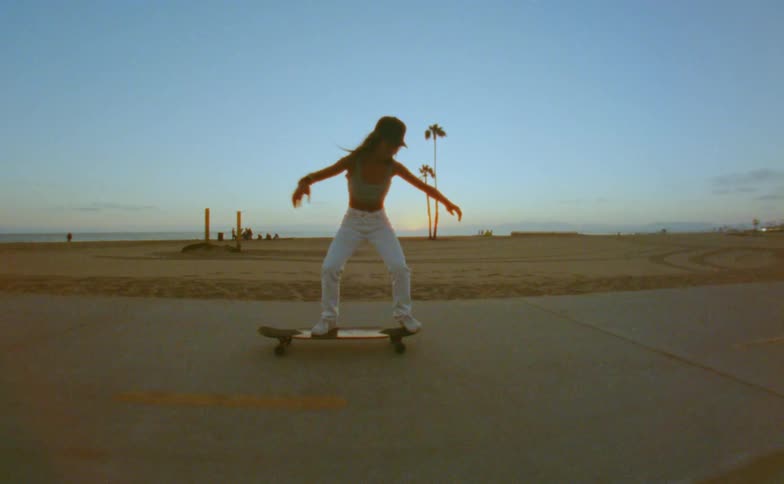 A woman in workout clothes is skateboarding down a sidewalk in a nonresidential area