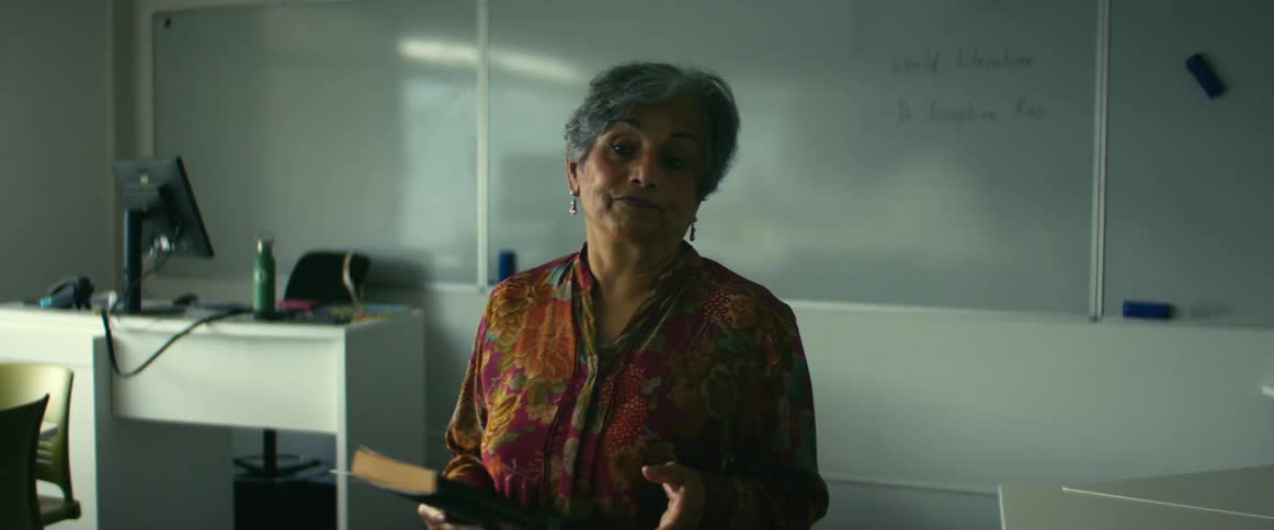 Professor with gray hair and red dress gives lecture in classroom
