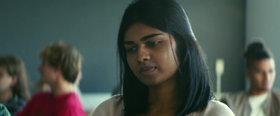 College student with straight hair sitting at desk smirks and wait for lecture in the class