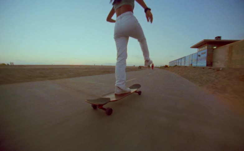 A woman rides a skateboard along a path on the beach