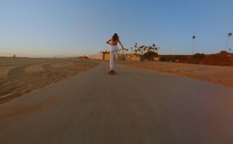 Young woman skateboards along paved path on beach in evening