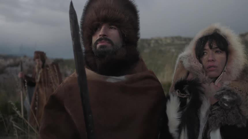 People in heavy clothing and fur pelts stand looking pensive