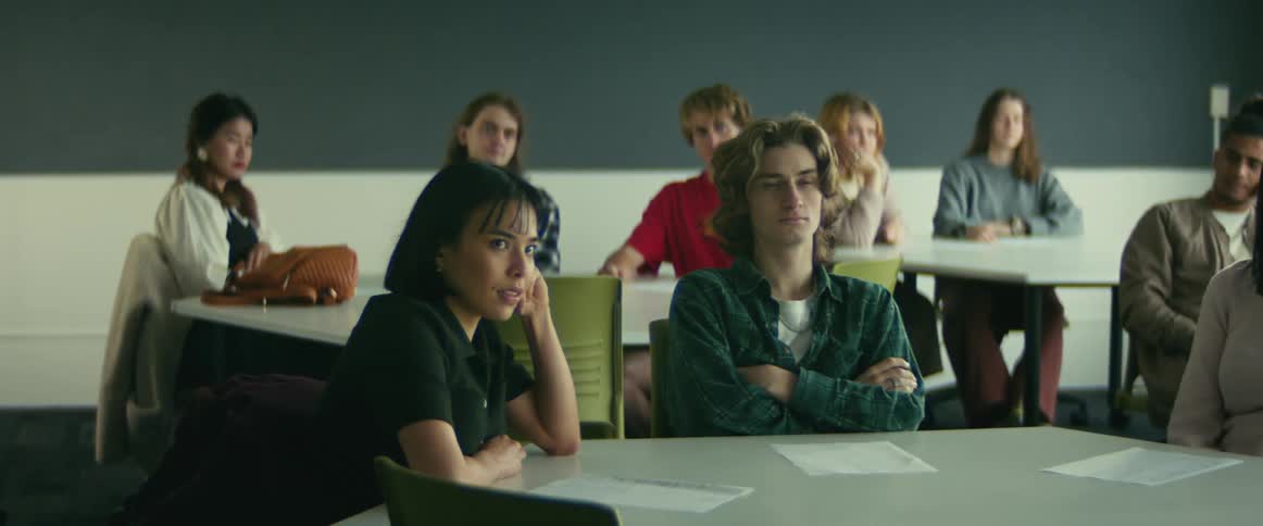 Students face the front of a classroom while sitting at large tables