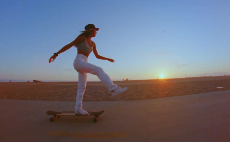 A woman skateboards down a flat road during sunset