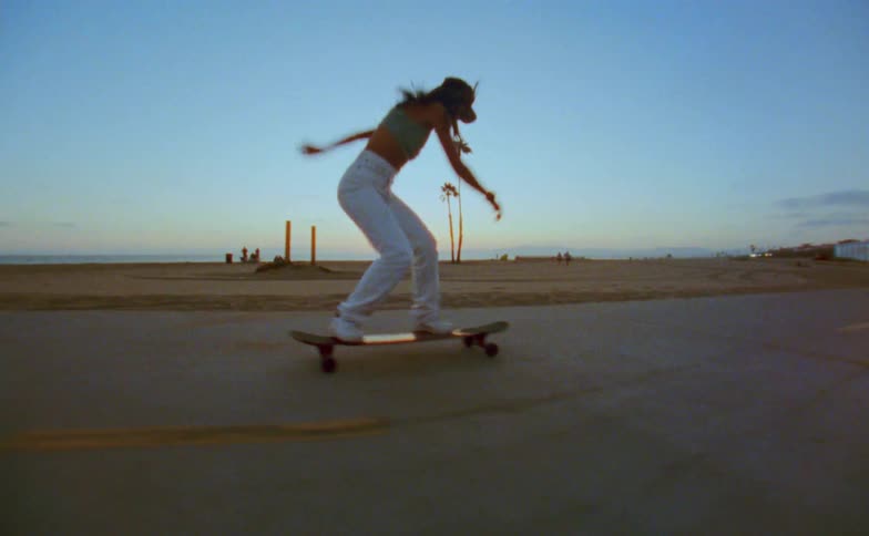 A woman is riding a skateboard and doing tricks on a path at the beach