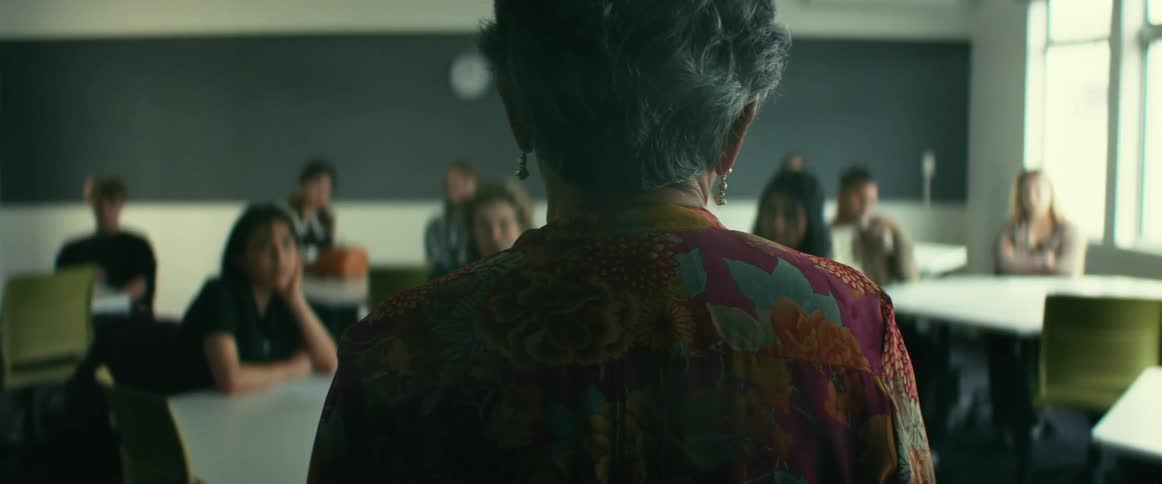 Female instructor gives a lecture while standing in classroom of students sitting at tables