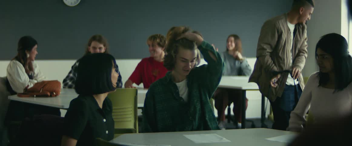 Students smiling and talking as they take their seats at group tables in a classroom