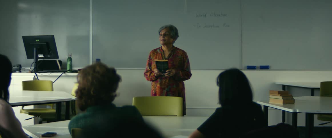 College students sitting at desks listen to professor giving lecture in front of whiteboard in class