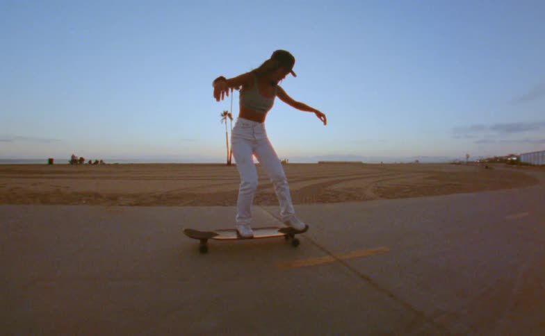 Woman skateboards down a road near a beach