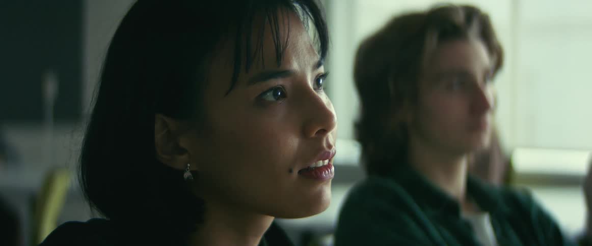 Camera slowly zooms out from a female student listening to a lecture and gently nodding