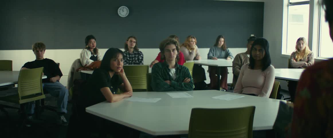 A professors stands in front of a classroom of students sitting around tables in a university classroom