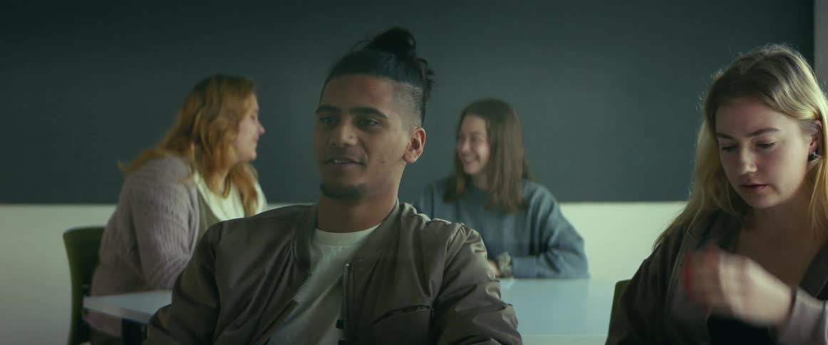 College students sitting at desks talk to each other in classroom