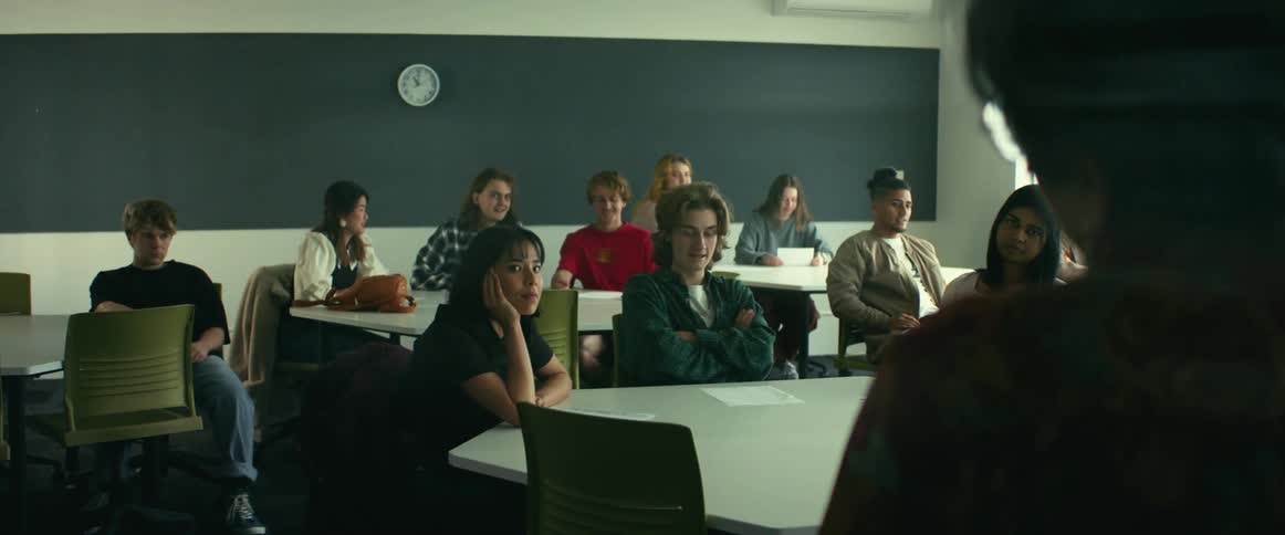 Teach stands in front of students sitting at large tables and lectures