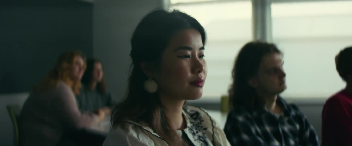 Asian woman sitting in the classroom with other students listening to the teacher talking