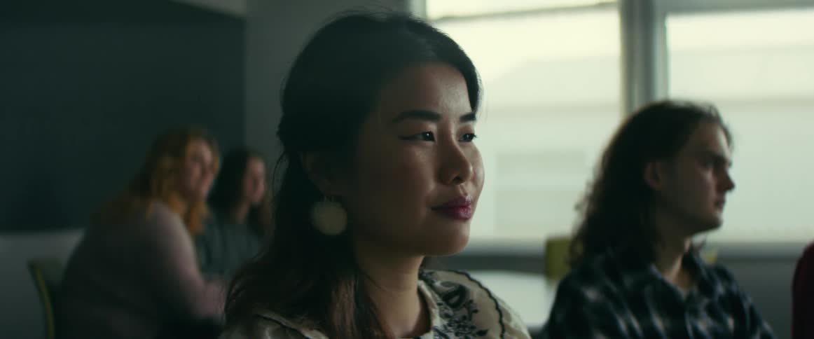 Asian woman sitting at the desk in a classroom with other students watching a class