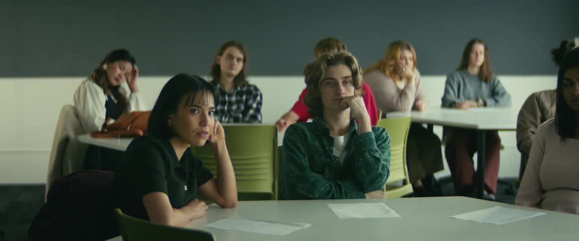 Students are sitting at tables with papers in a classroom
