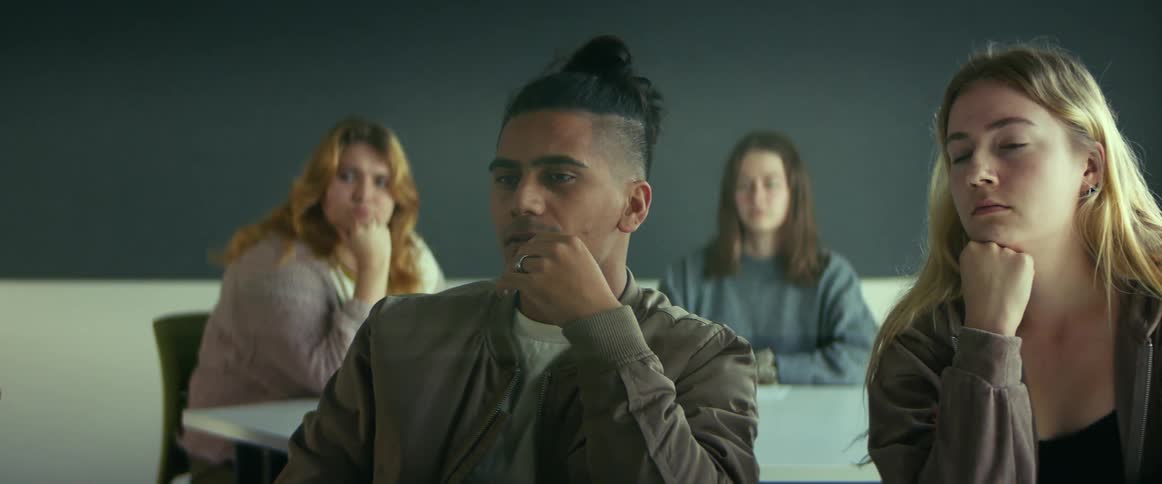A group of people sits quietly at tables in a room