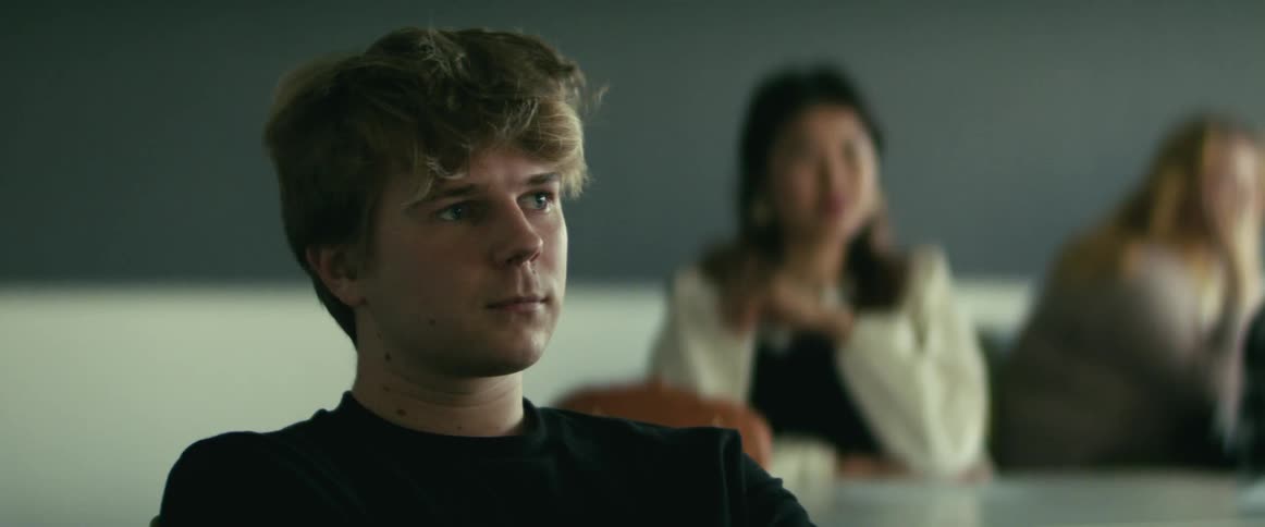A teenage boy sits in a classroom looking at someone up front