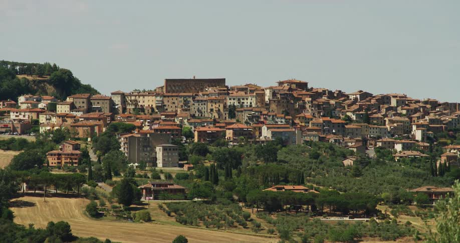Crop fields border red roofed buildings of town sitting on hills