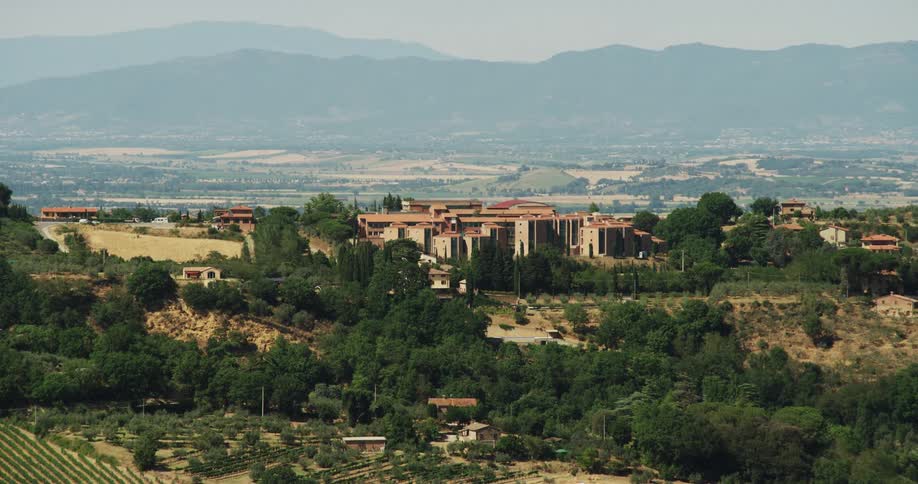 Town buildings stand between crop fields with fog covered mountains on the horizon
