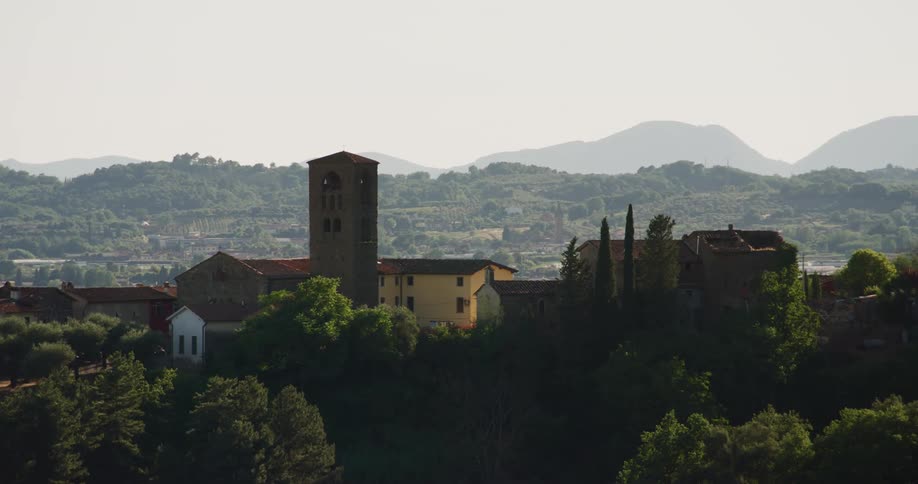 Building with bell tower sits on hill overlooking town bordered by mountains on misty day