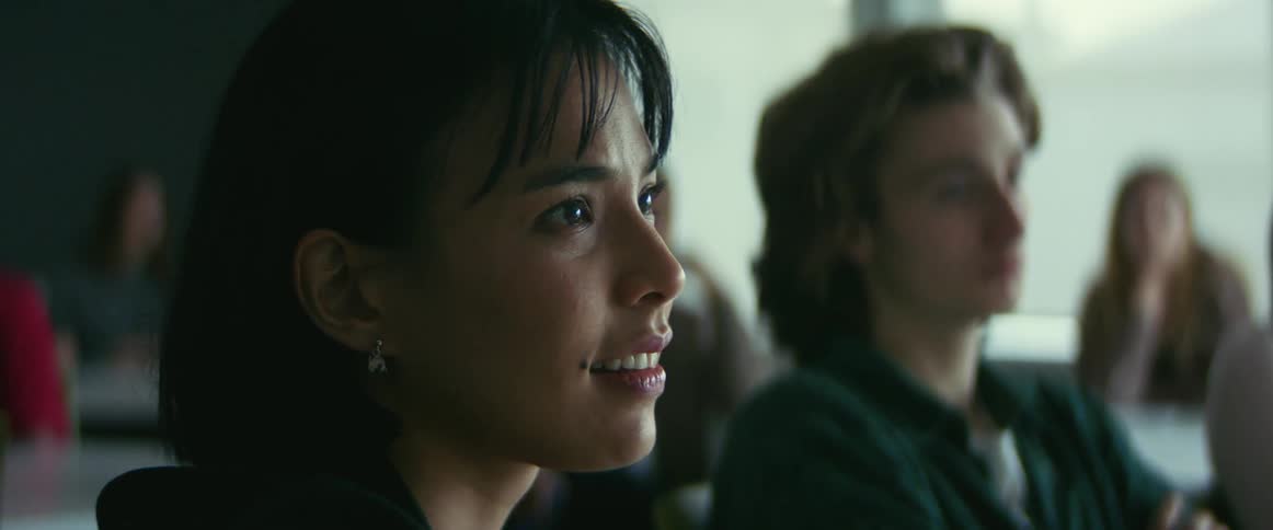 Camera slowly zooms in on a female student as she smiles while listening to a lecture