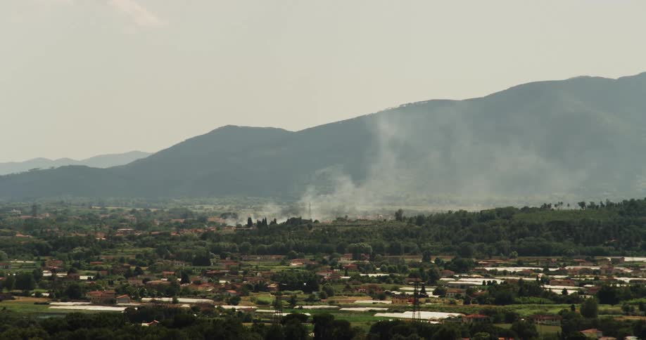 Smoke slowly passes by a mountain range over a town